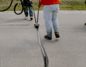 Two workers fill a crack with asphalt materials.